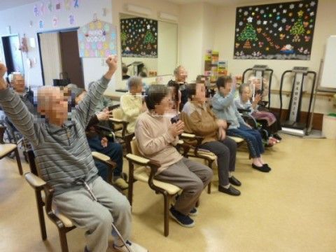 肘掛つきの椅子に座り、手をたたいたり、手をあげながら楽しむ入居者