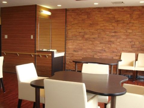 奥の方に洗面台が広い部屋。四つ葉のクローバーのような形の茶色いテーブルがあり、その周りに白い椅子が置かれている。