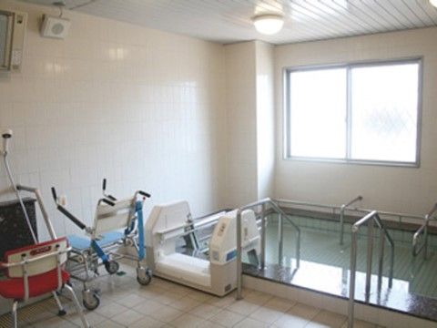 介助用の椅子などが置かれている浴室。浴槽は広めで、プールのような鉄製の手すりが両側に設置されている。