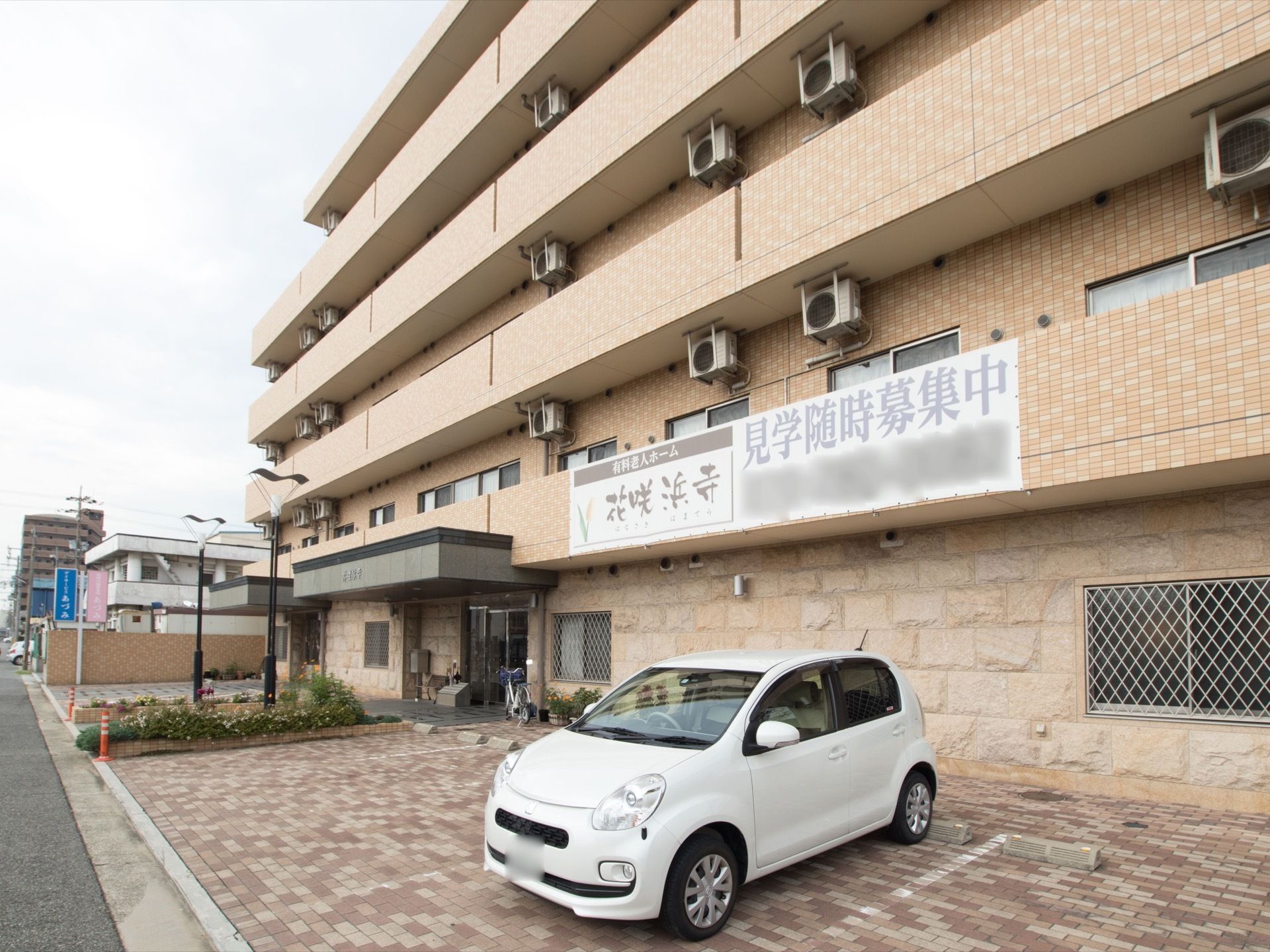 オレンジのタイルが貼られた５階建ての施設である。施設前は駐車スペースがあり、白い乗用車が１台停まっている。
