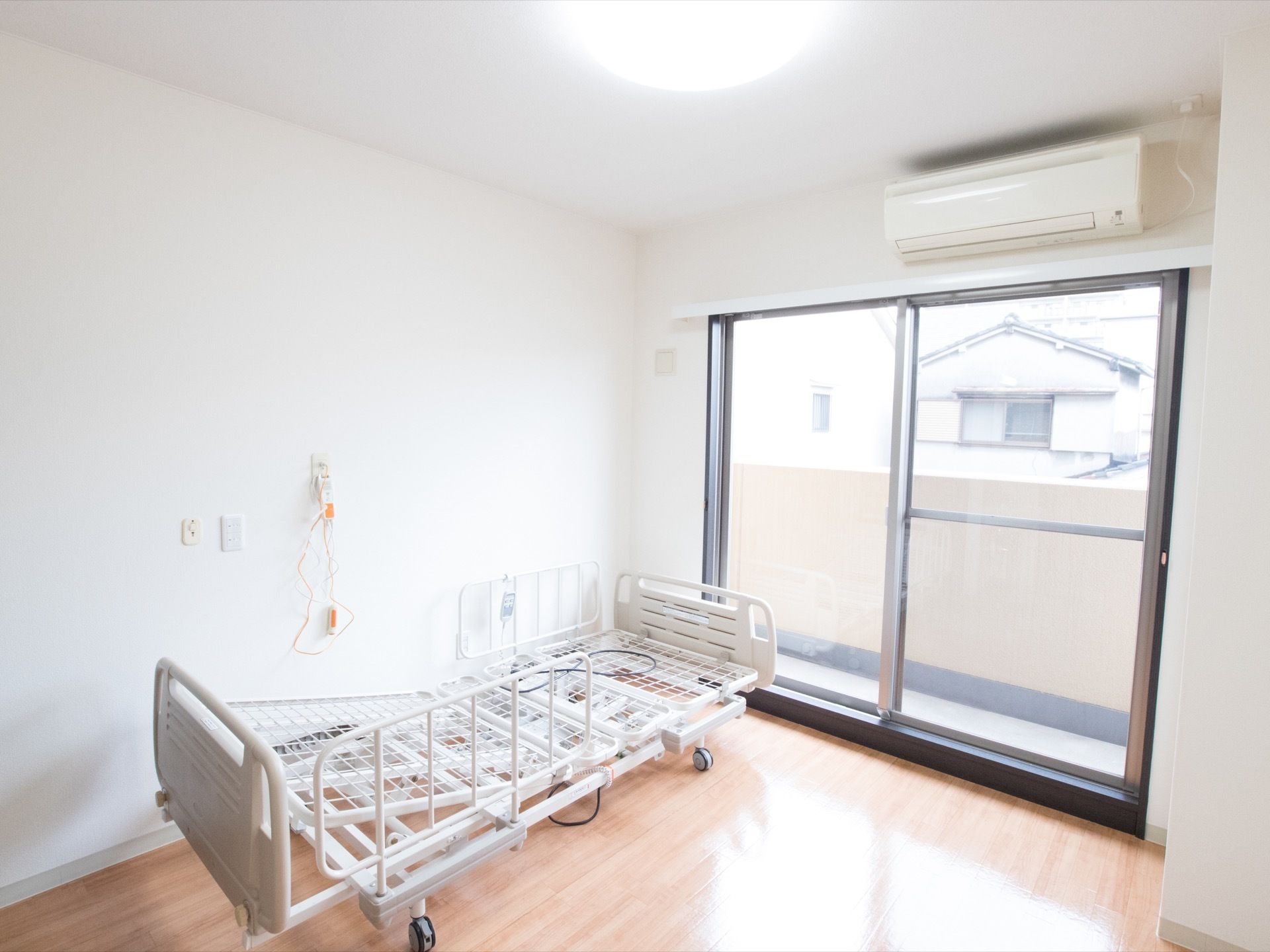 居室には大きな窓があり、ベランダへ出ることができる。窓の上にはエアコンが設置されている。壁側にベッドが置かれている。