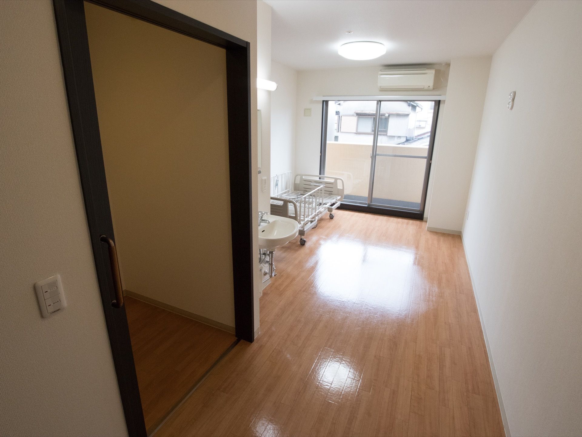 居室はトイレと洗面台が完備されている。床はフローリングでバリアフリーとなっている。奥にベランダへ出る窓がある。