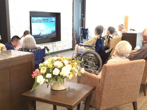 バラの花が飾られたリビングのソファーに利用者様が集まってテレビを見ている様子