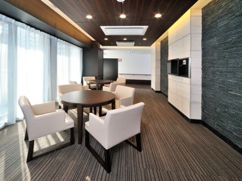 落着いた色調の空間の窓辺には、茶色の丸テーブルと白い椅子が置かれ、カーテン越しに太陽光が差し込んでいる。