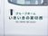 施設の車である。白いバンのスライドドアに、緑色の文字で施設名と電話番号が書かれている。ドアの取っ手は黒色である。