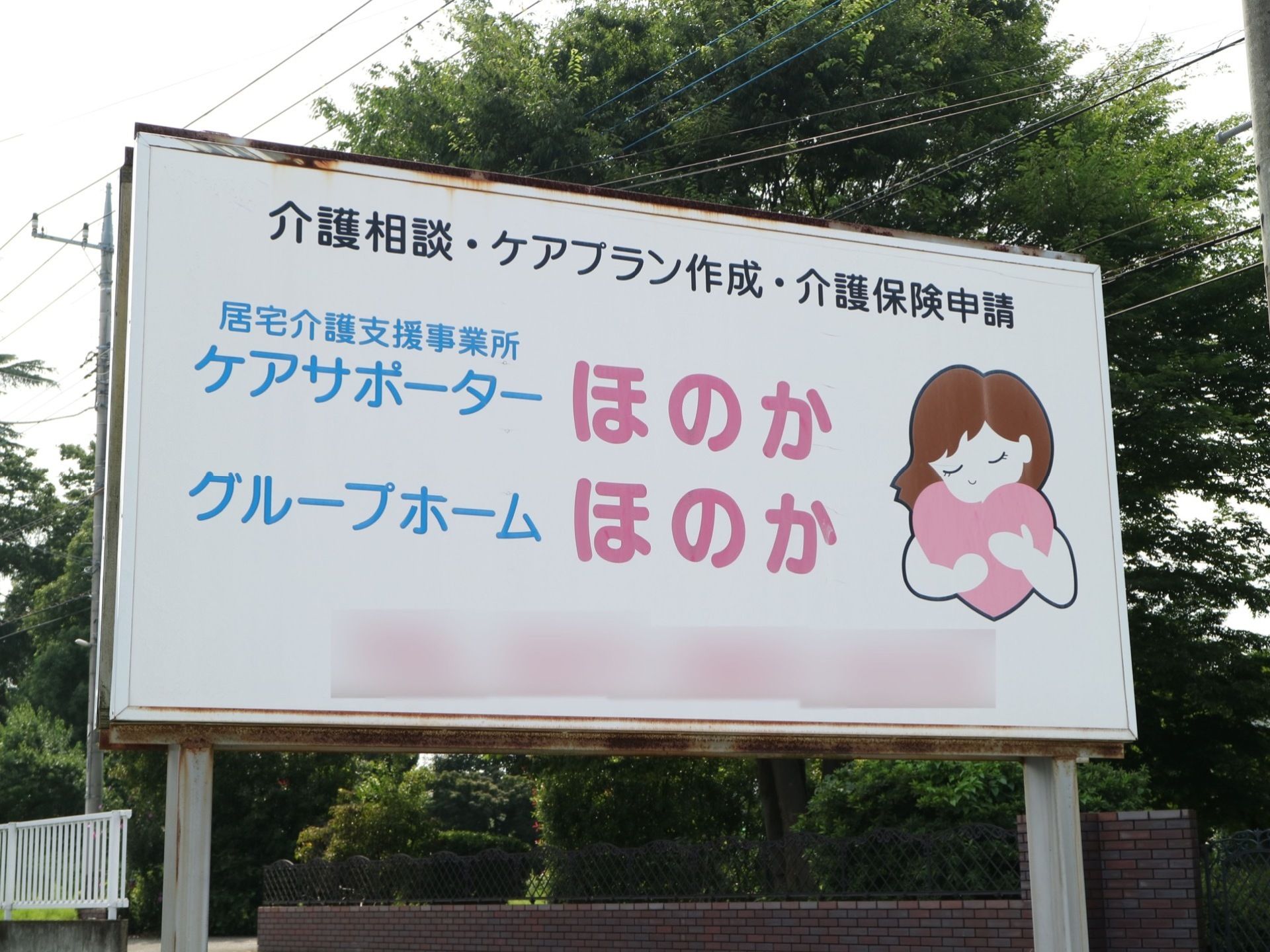 施設の外に大きな看板が立てられている。白い板に女性のイラストが描かれ、ピンクや水色の文字で施設名が書かれている。