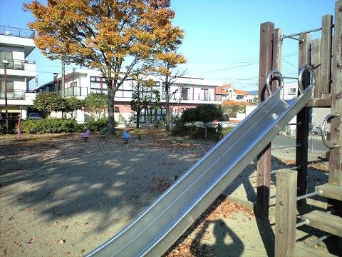 奥に大きな木があり、手前には滑り台などの遊具がある場所