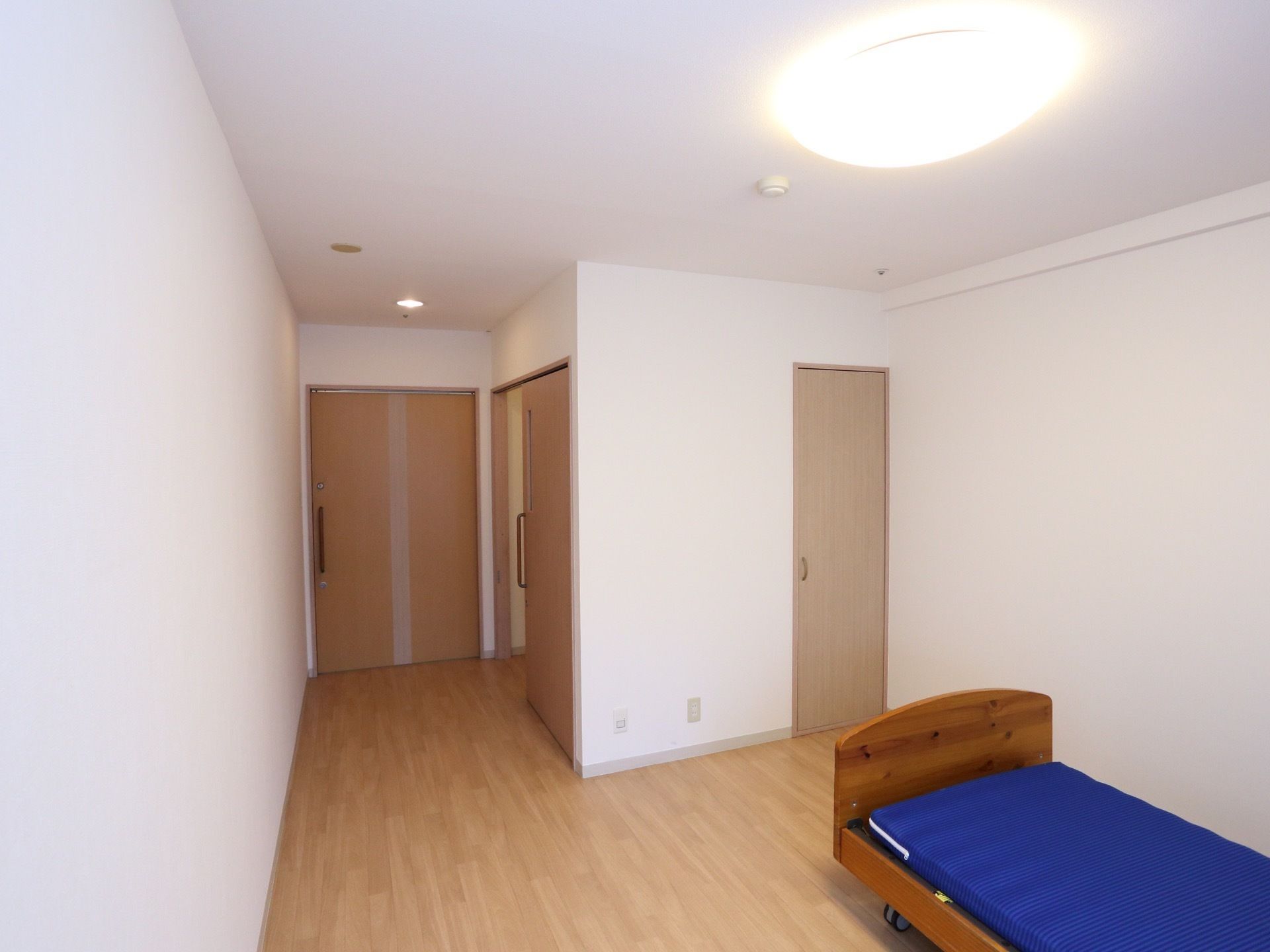 部屋の扉は引戸で、大きく開くようになっている。足元はバリアフリー。壁側にはベッドが置かれている。備付の収納がある。