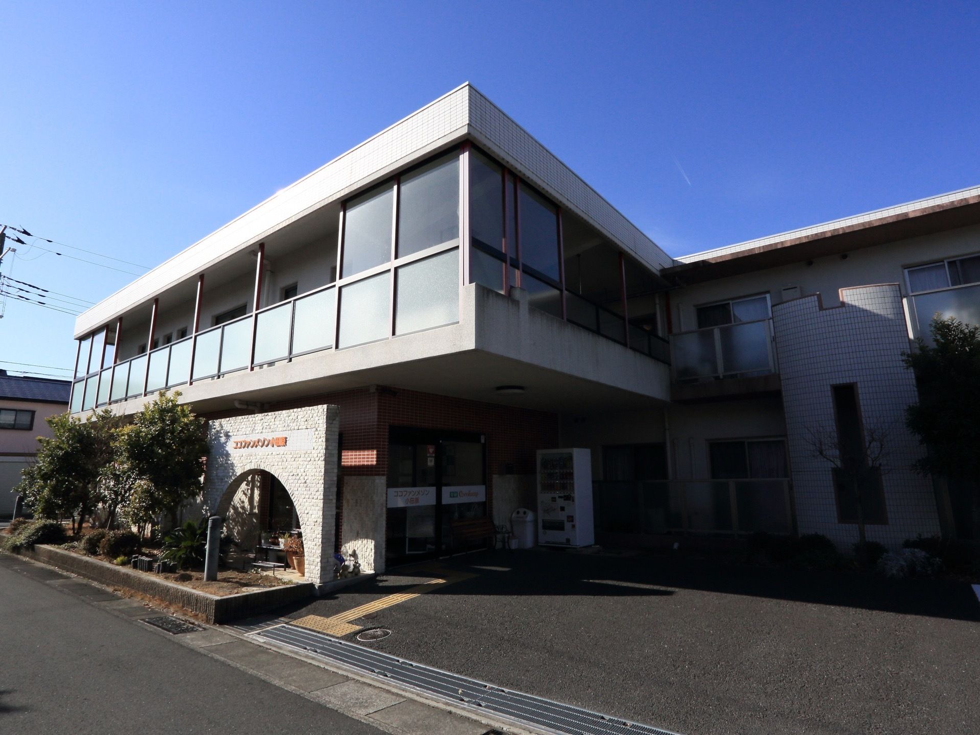 施設は２階になっている。２階部分にはベランダが設置されている。玄関扉の横には、自動販売機が設置されている。