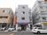周りの街並みに溶け込む外観の施設。4階建てで、グレーの外壁である。玄関前には自動販売機が置かれ、3台分の駐車スペースがある。