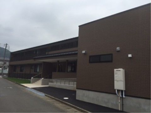 ダーク系の落ち着いた外観である。建物は２階建て。スロープのとなりは緑地が整備され、清潔感ある雰囲気である。