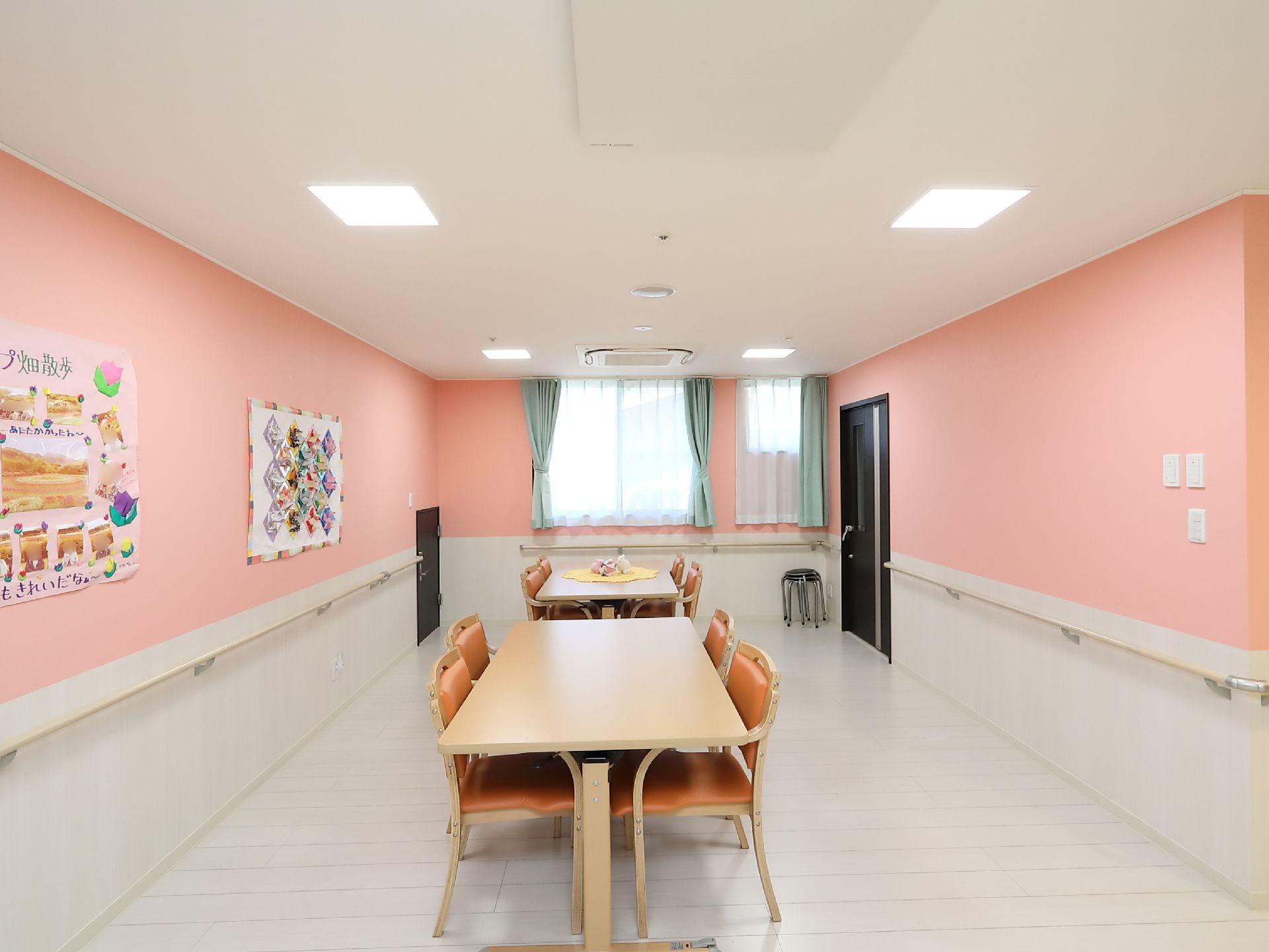 縦長の部屋である。腰高以上の壁は淡いオレンジ色に、腰高以下と床は白い色でまとめられている。中央にテーブルセットが2つある。