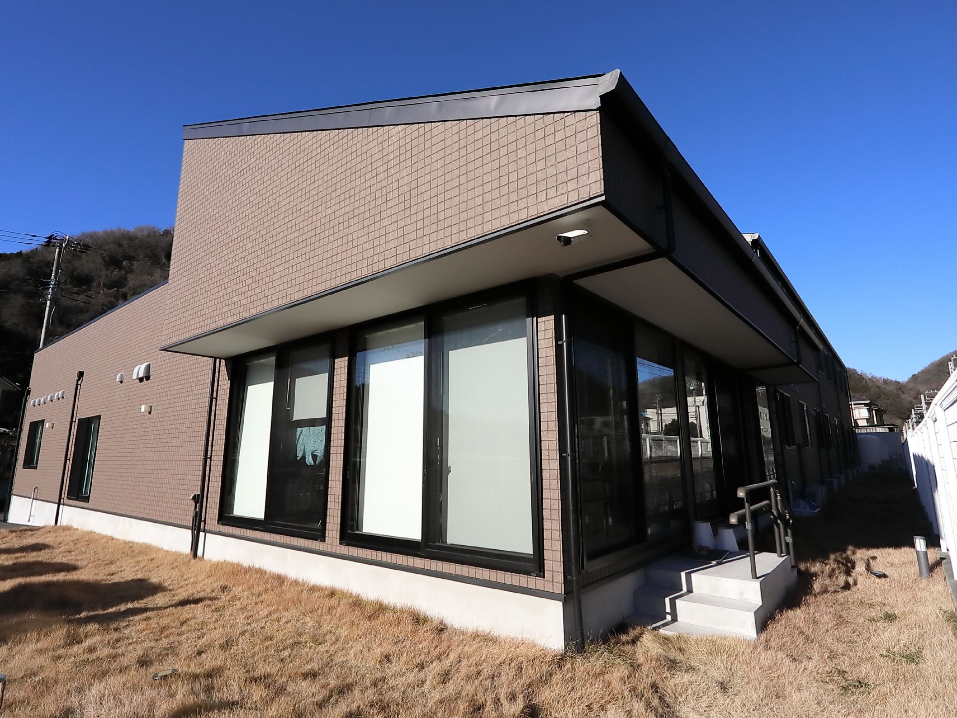 1階に掃き出し窓があり、屋外へ出るための手すりつきの階段がある。建物を囲むように芝生が植えられている。