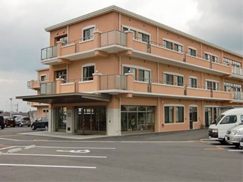 広い駐車場と玄関前にひさしのあるオレンジ色の壁の３階建ての建物