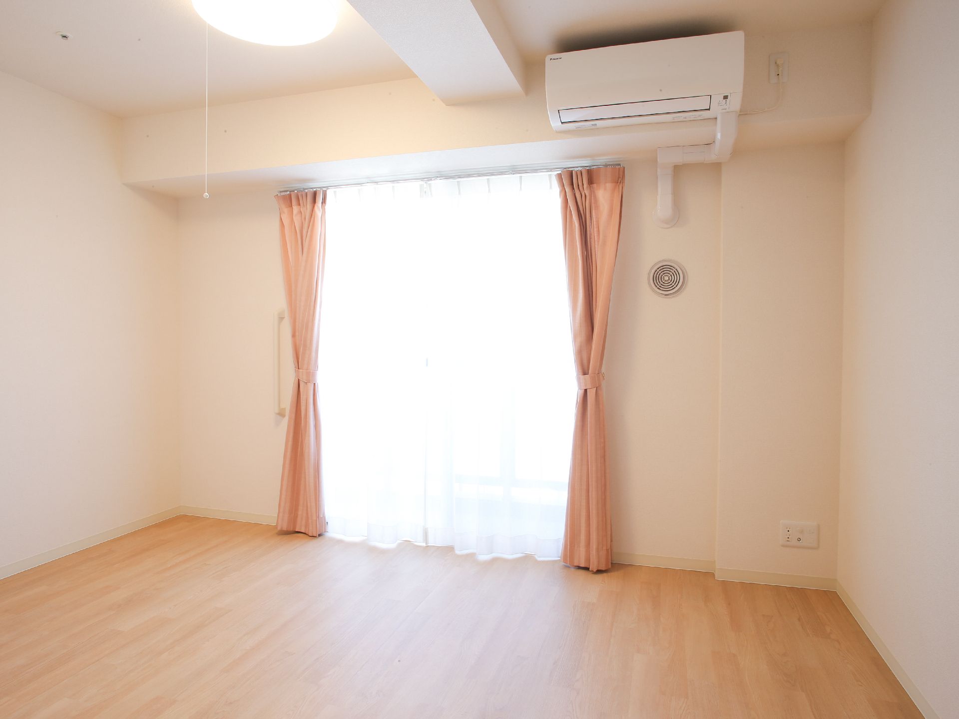 大きな窓にピンクのカーテンが掛かったエアコン付きのフローリングの部屋