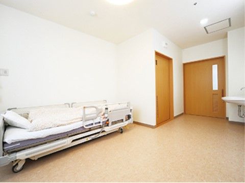 居室の入り口には引き戸が設けられ、壁には洗面台が設置されている。トイレは引き戸で区切られ、介護用のベッドが置かれている。