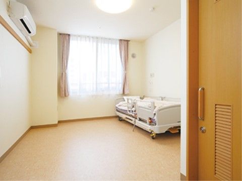 居室には窓があり、壁と天井は白色基調である。床には介護用ベッドが設置され、広いスペースが確保されている。