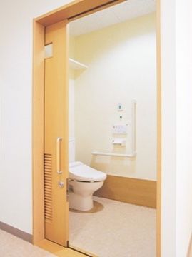 居室のトイレは引き戸で区切られており、温水洗浄便座が設置されている。便座の近くには手すりが設けられ、周囲には広いスペースが確保されている。