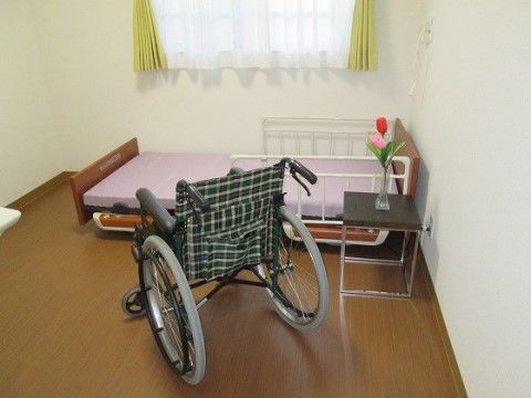 リクライニングベッドと車いす、サイドテーブルにチューリップの花が飾られてる部屋