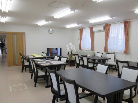 黒いテーブルと、グレーの座面に黒枠の椅子が並ぶリビング。窓にかけられたピンクのカーテンが、空間に彩りを添えている。