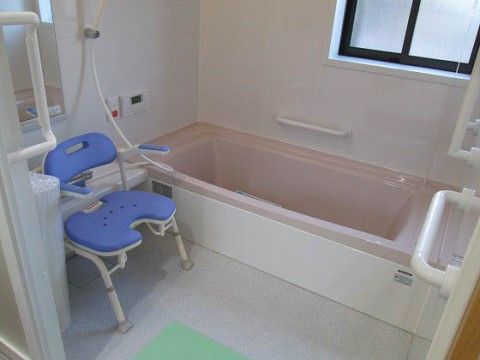白い壁に淡いピンクのバスタブがやすらぎを与えてくれる浴室。洗い場にはどっしりとしたひじ掛け付きの椅子が置かれている。