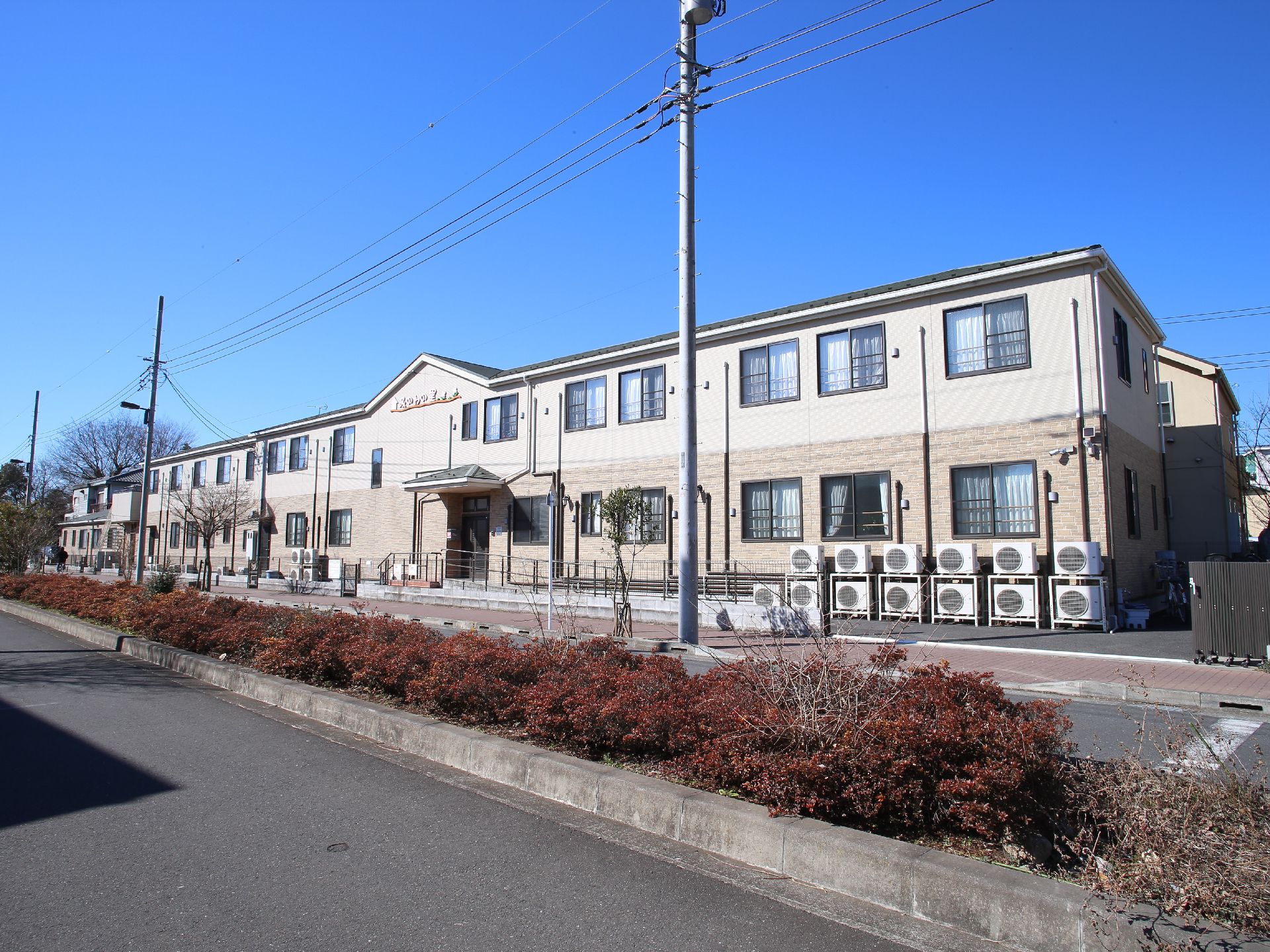 リゾートホテルのような2階建ての横長の建物。周辺は緑があり閑静な立地。建物周辺にスペースが十分ある。