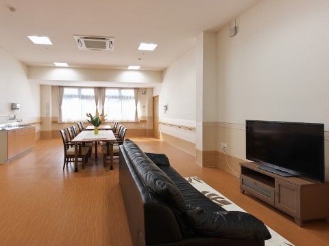 大型テレビの前に、黒い皮張りのゆったりと座れるソファーが置かれている。奥には花が飾られたテーブルと椅子も置かれている。
