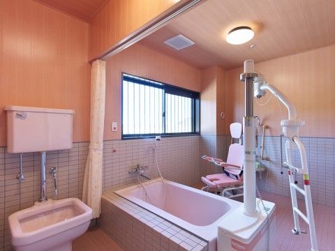 窓から天然光が差し込む浴室。入浴に介助が必要な方も安心して入れるリフト装置が、浴槽の横に置かれている。