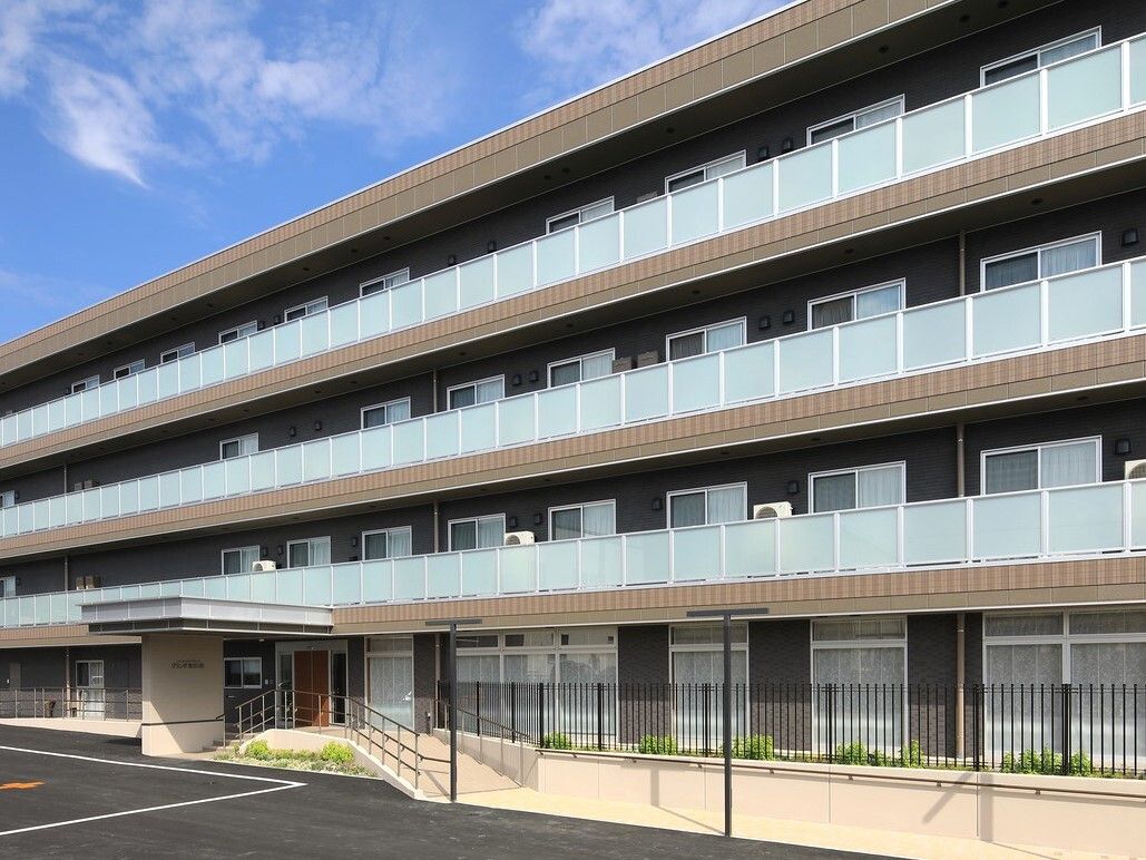 4階建ての建物で、前にコンクリート舗装された広い敷地がある外観