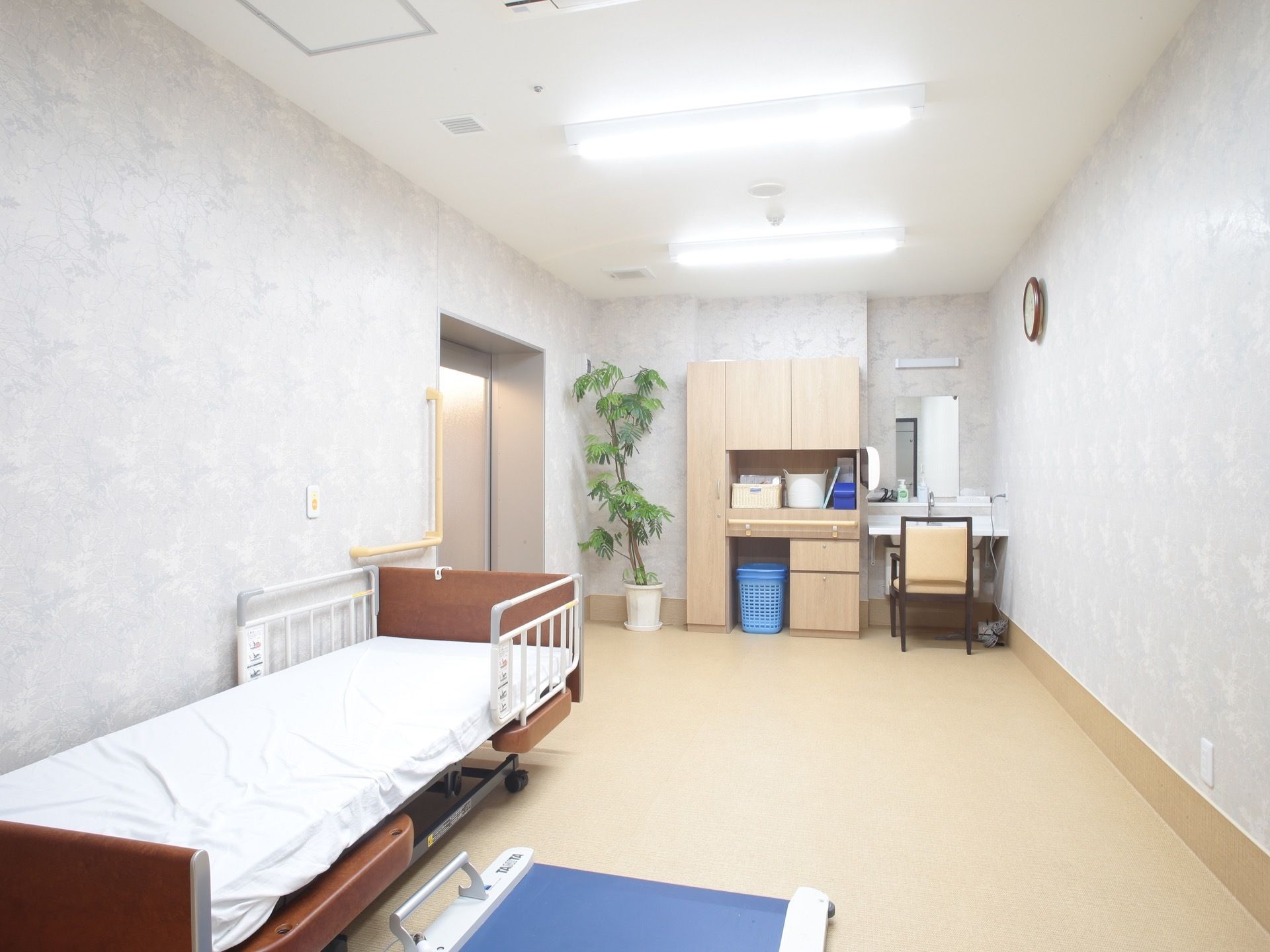 壁面に介護用移動式ベッドと車椅子に乗ったまま測れる体重計を備えた健康管理室