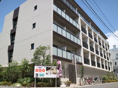 大きな施設建物を下から見上げたところ。鉄筋コンクリートの頑丈なつくりになっている。道路との間には植え込みがある。