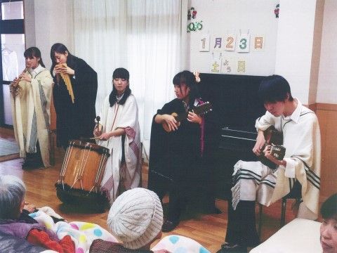 マントを羽織り演奏する５人の若者の音楽を聴く、入居者の方々