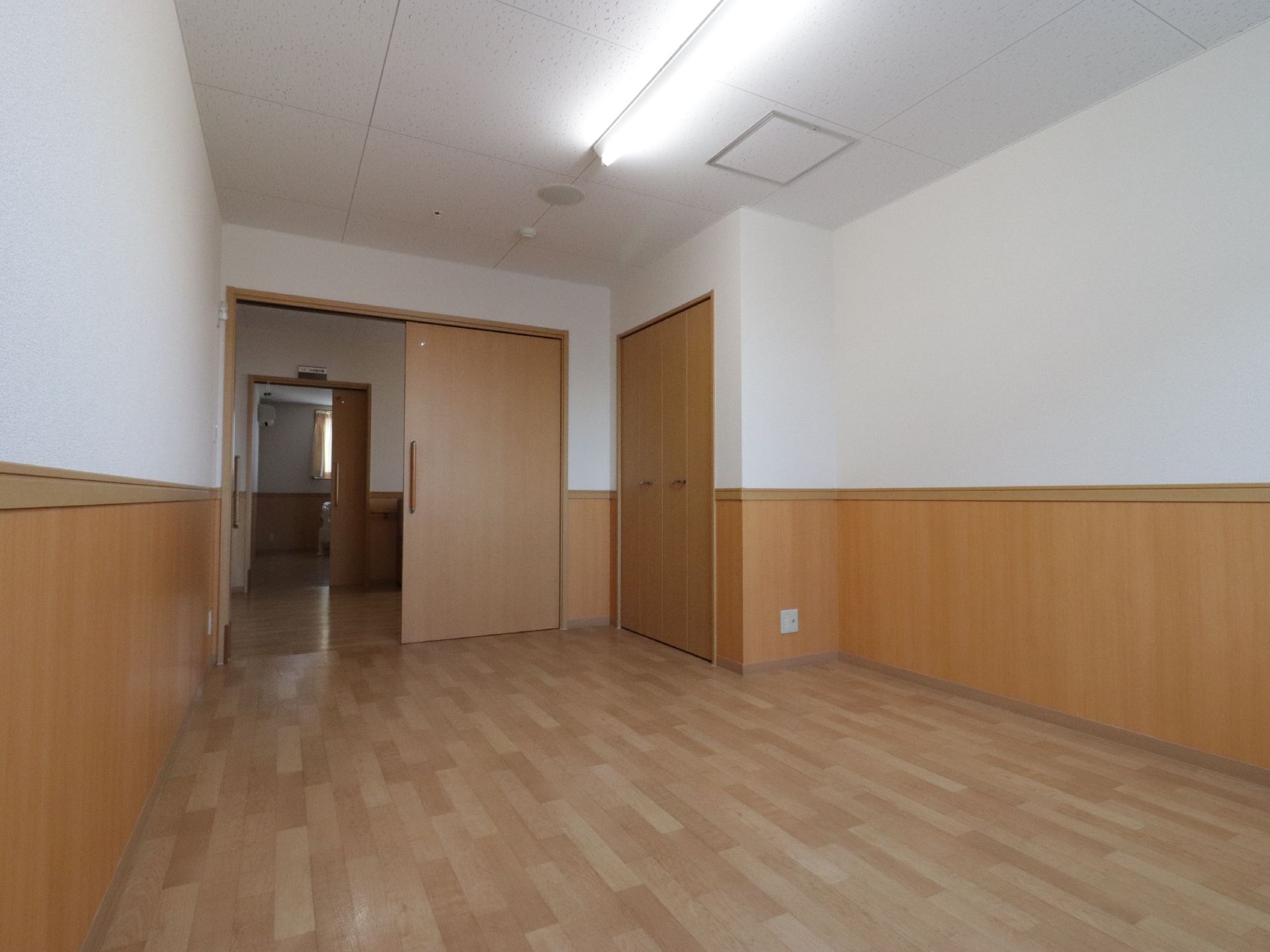 広々としたスペースが確保されている居室である。出入り口の引き戸が全開になっており、通路の向こうの部屋の中が見える。