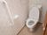 壁は花柄模様である。清潔感のある個室トイレで、洋式便座が1台設置されている。右側の壁に縦型の手すりが取りつけられている。