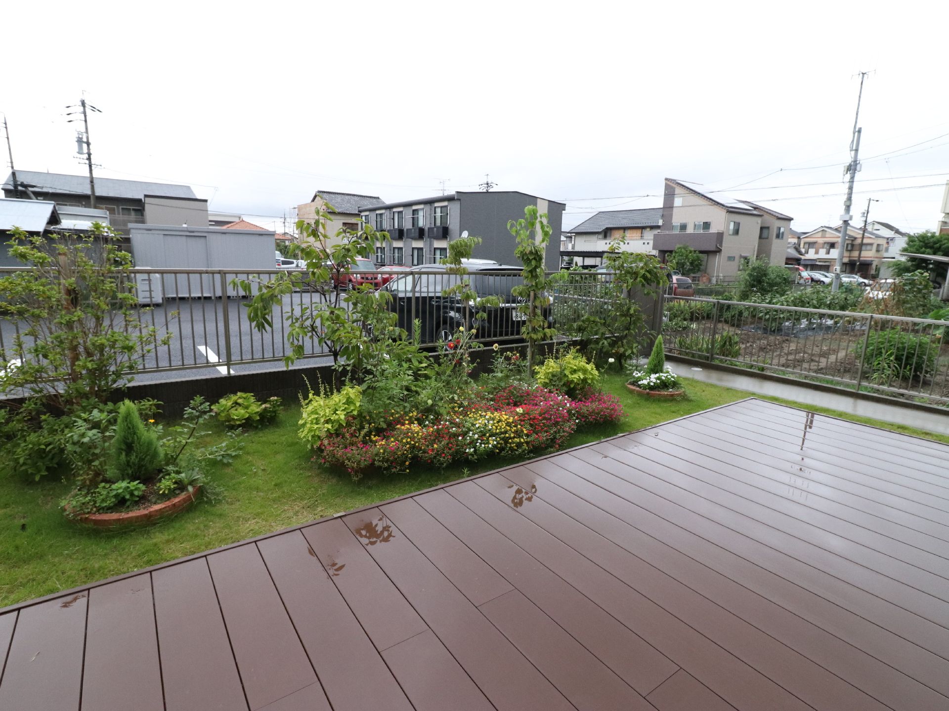 施設の外周は金属製のフェンスで囲われている。フェンスの外は施設の駐車場で、右側には畑がある。周辺は住宅地である。