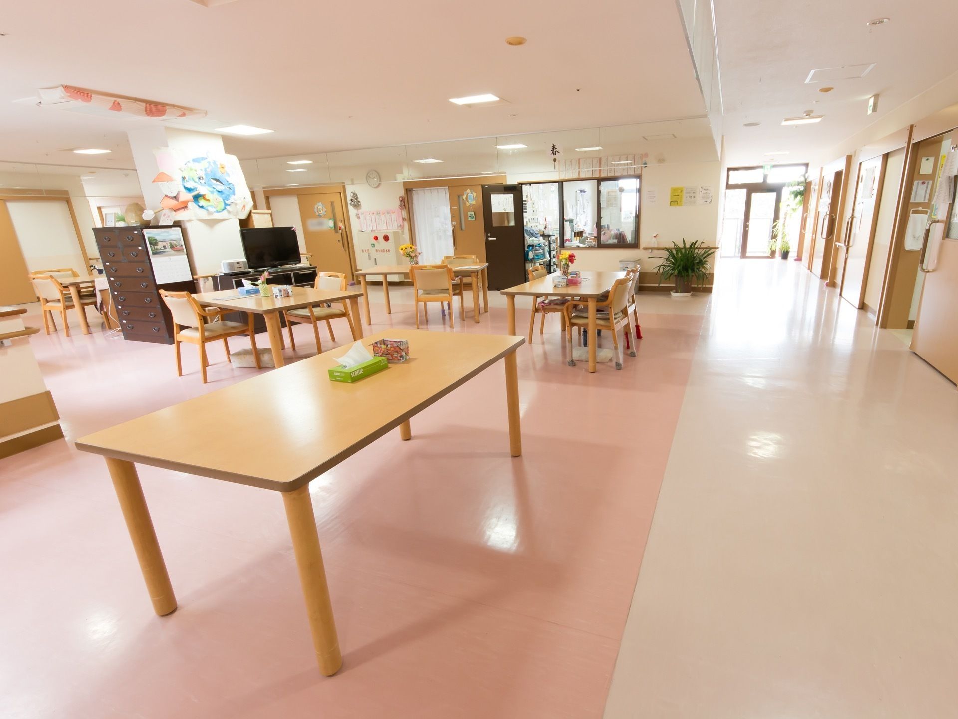 リビングと居室は隣接しており、入居者様が利用しやすくなっている。廊下の突き当りにある扉からは、光が差し込み、とても明るい。