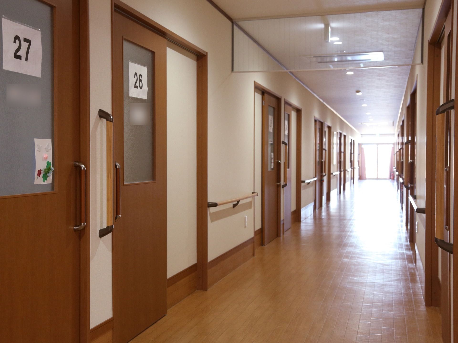 廊下はフローリングで、とても清潔で広くなっている。両側には居室があり、部屋番号が大きく貼られている。