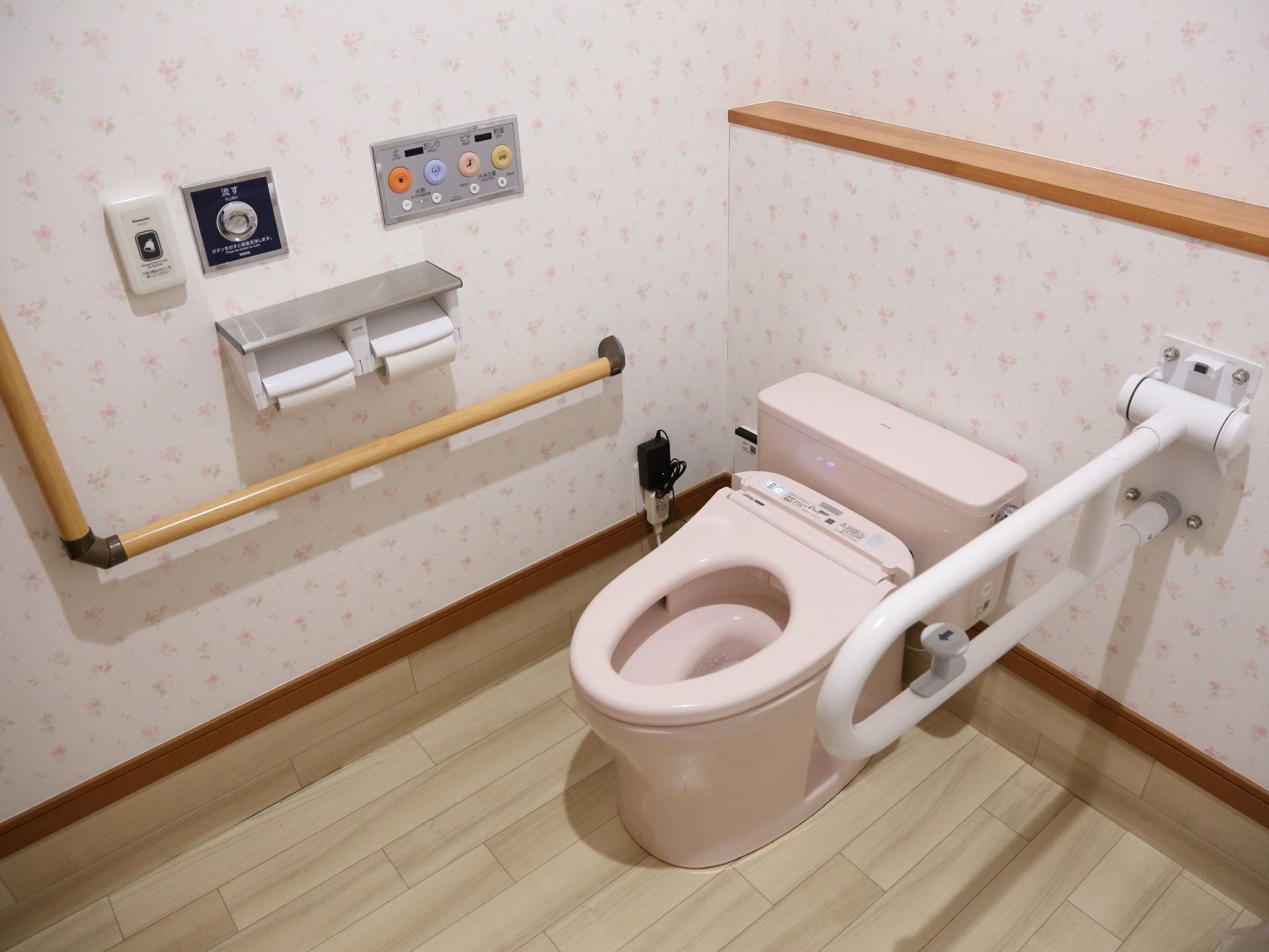 広々としたトイレには温水洗浄便座付きの便器が設置されている。便器の横には可動式の手すりが付いている。