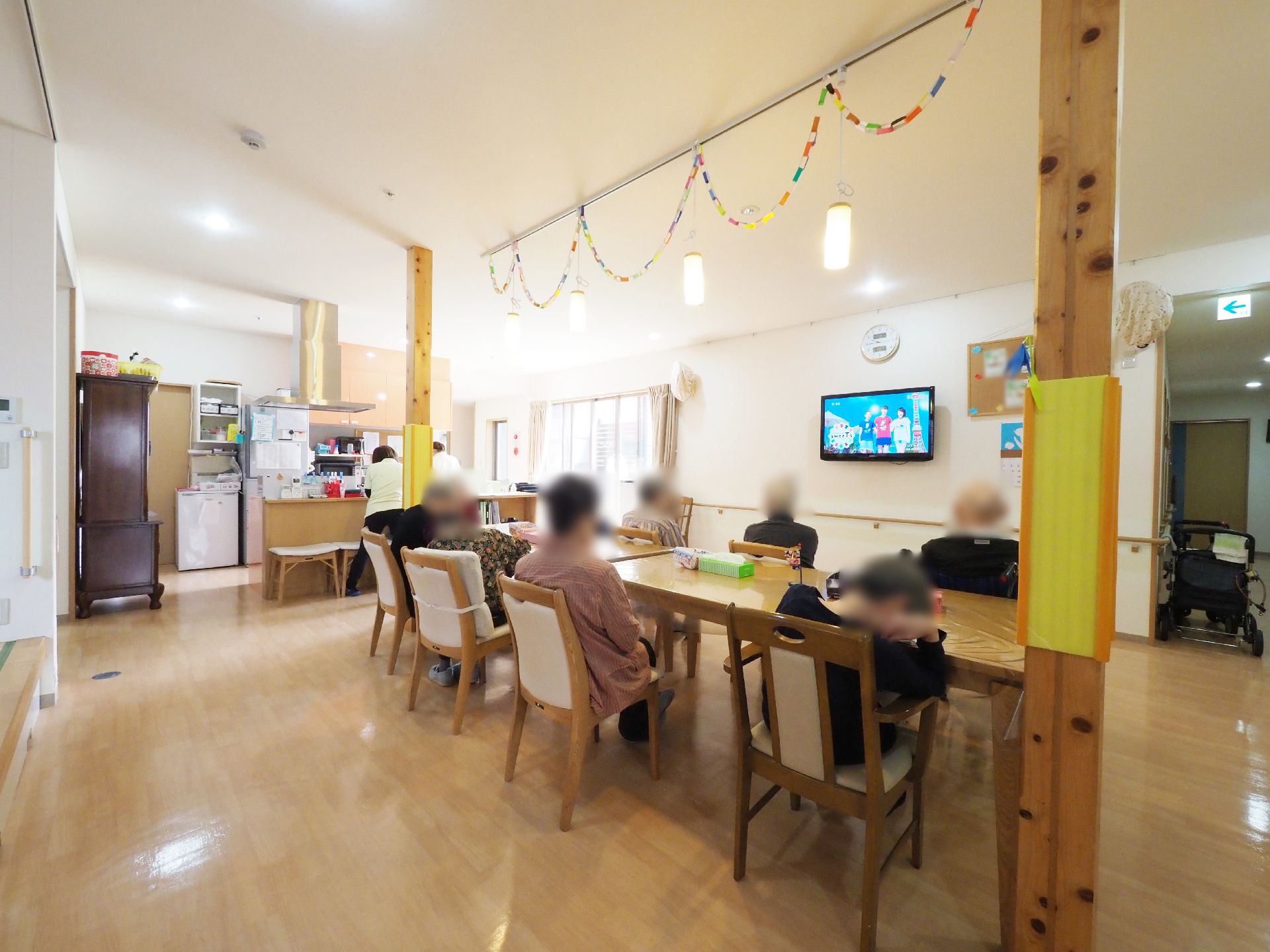 入居者様が揃ってテレビを観ている。テーブルは縦長に置かれていて、周りにはゆとりのあるスペースがある。