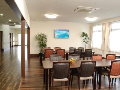 観葉植物が２つならんでいる広々とした場所で、沢山の机と椅子が並んでいる室内
