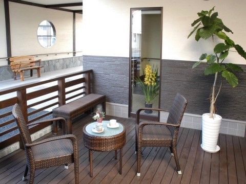 奥には丸形の窓と木材を使用ベンチがあり、手前には観葉植物とベンチ、机と２脚の椅子がある空間