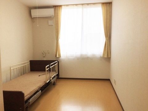 正面にガラス窓があり、介護用ベッドが備え付けられたエアコンがある居室