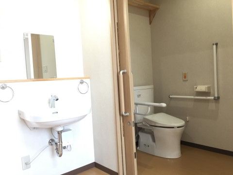手前に洗面台があり、奥に洗浄機能付きのトイレが設置されている。トイレの壁には入居者様の安全確保のために手すりが取り付けてある。