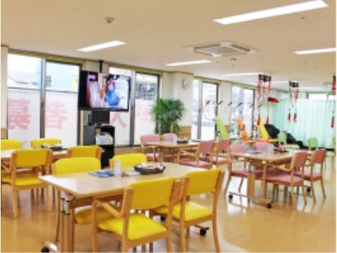 黄色とピンク２種類の椅子とテーブルが４ヶ所に配置されたテレビのある食堂