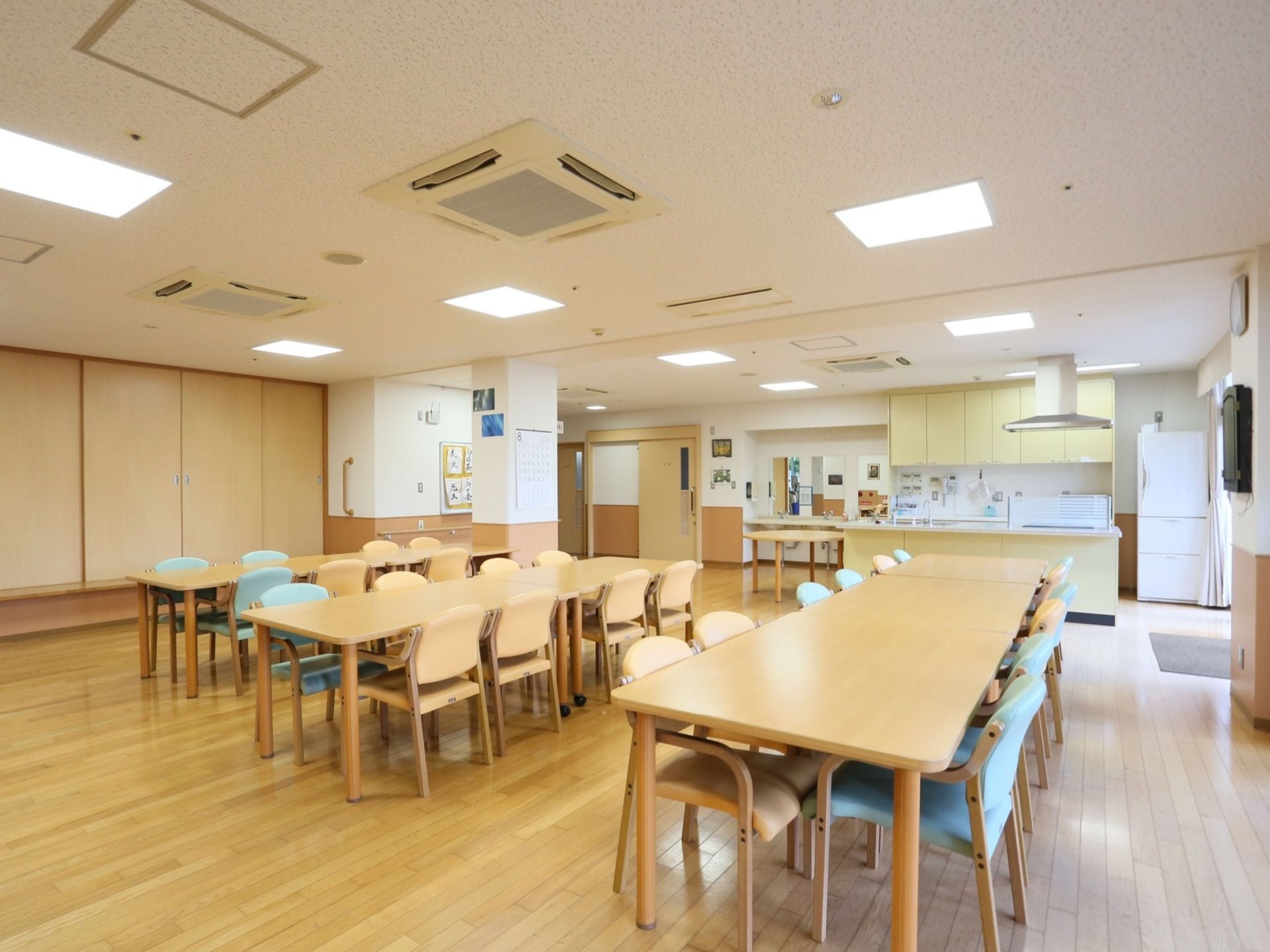 食堂も兼ねた多目的ホール。食事以外もレクリエーションや、入居者様が各々楽しめるように明るい色合いの広いテーブルが設置されている。