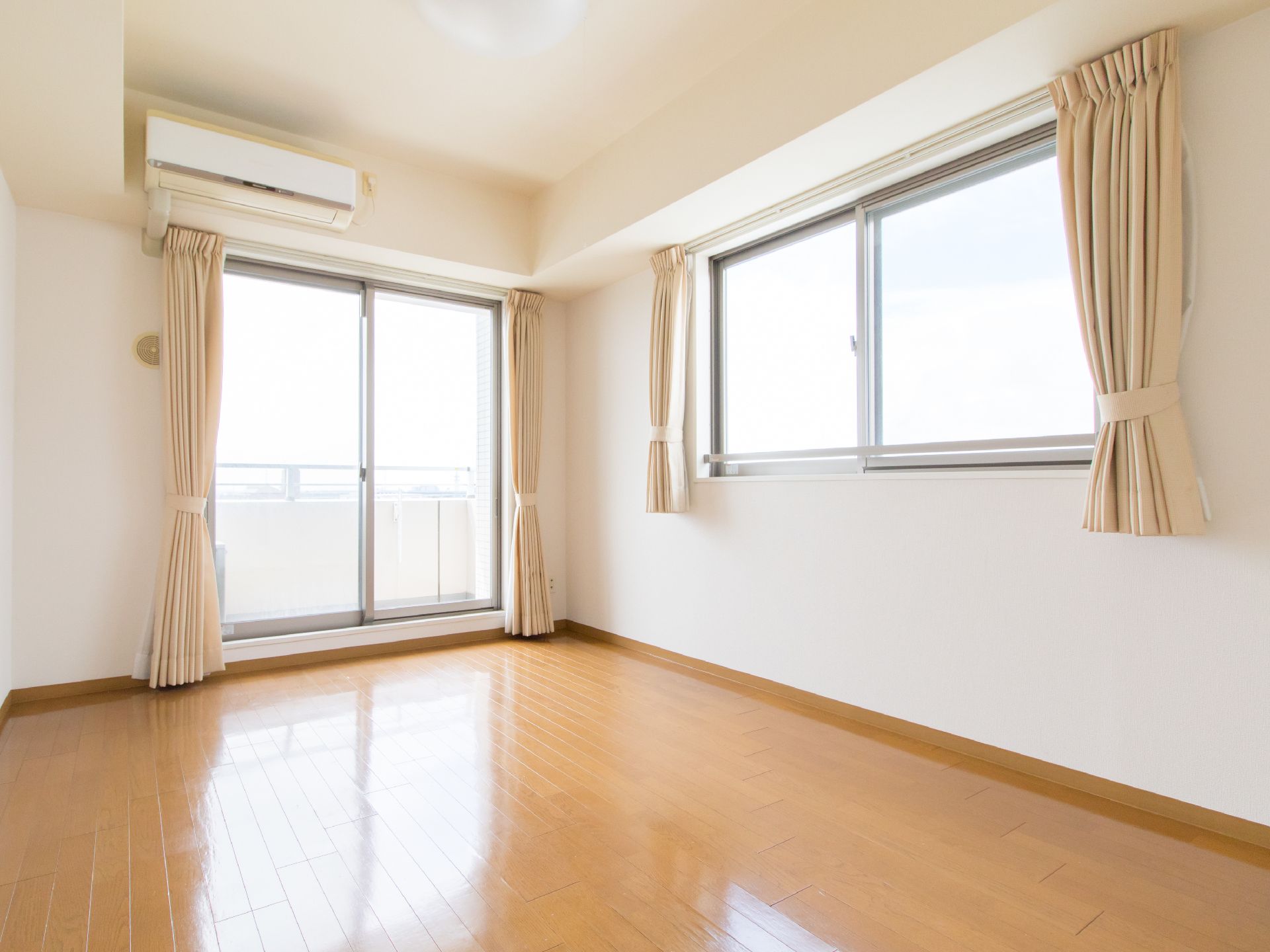居室内の壁には掃き出し窓と腰高窓が1つずつあり、それぞれにダブルカーテンが掛けられている。床はフラットなフローリングである。