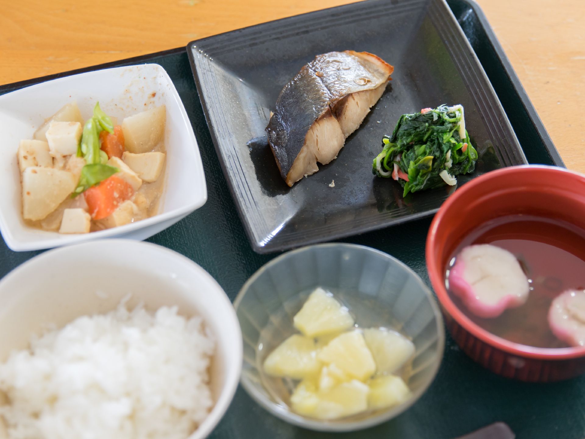 長方形のトレーの上に1人分の食事が並べられている。この日のメインは切り身の焼き魚で、野菜の煮物とフルーツが付いている。