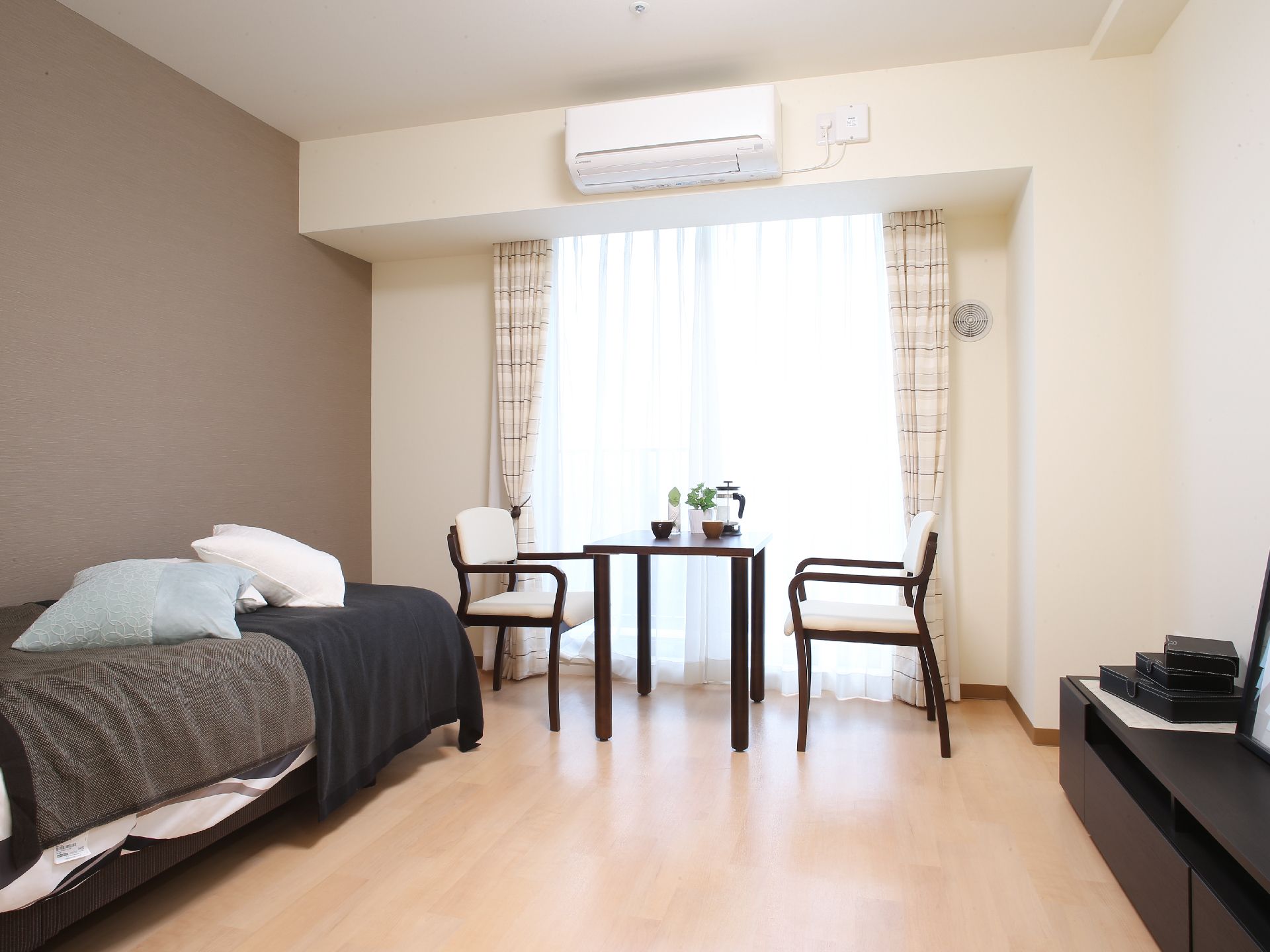1人用のシングルベッドが置いてある。部屋はダークブラウンで統一されている。テーブルと2脚の椅子がある。