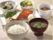 ご飯、お味噌汁、焼鮭、納豆、サラダ、小鉢というメニューの朝食の一例である。品数が多く、彩りも鮮やかである。