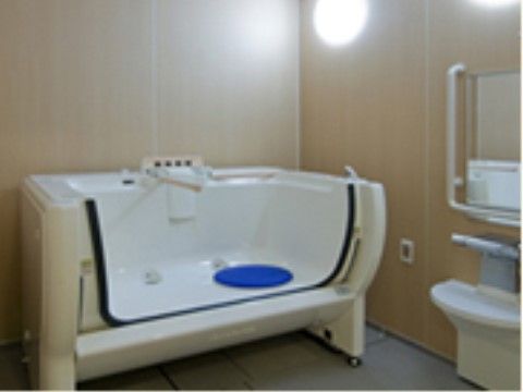 木目調の壁の浴室に、片側の壁が可動式の特殊な浴槽が置かれている。浴槽の近くの壁に、ナースコールが備わっている。